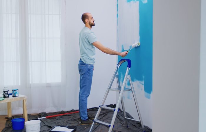 Handyman painting wall with roller brush dipped in white paint. Handyman renovating. Apartment redecoration and home construction while renovating and improving. Repair and decorating.